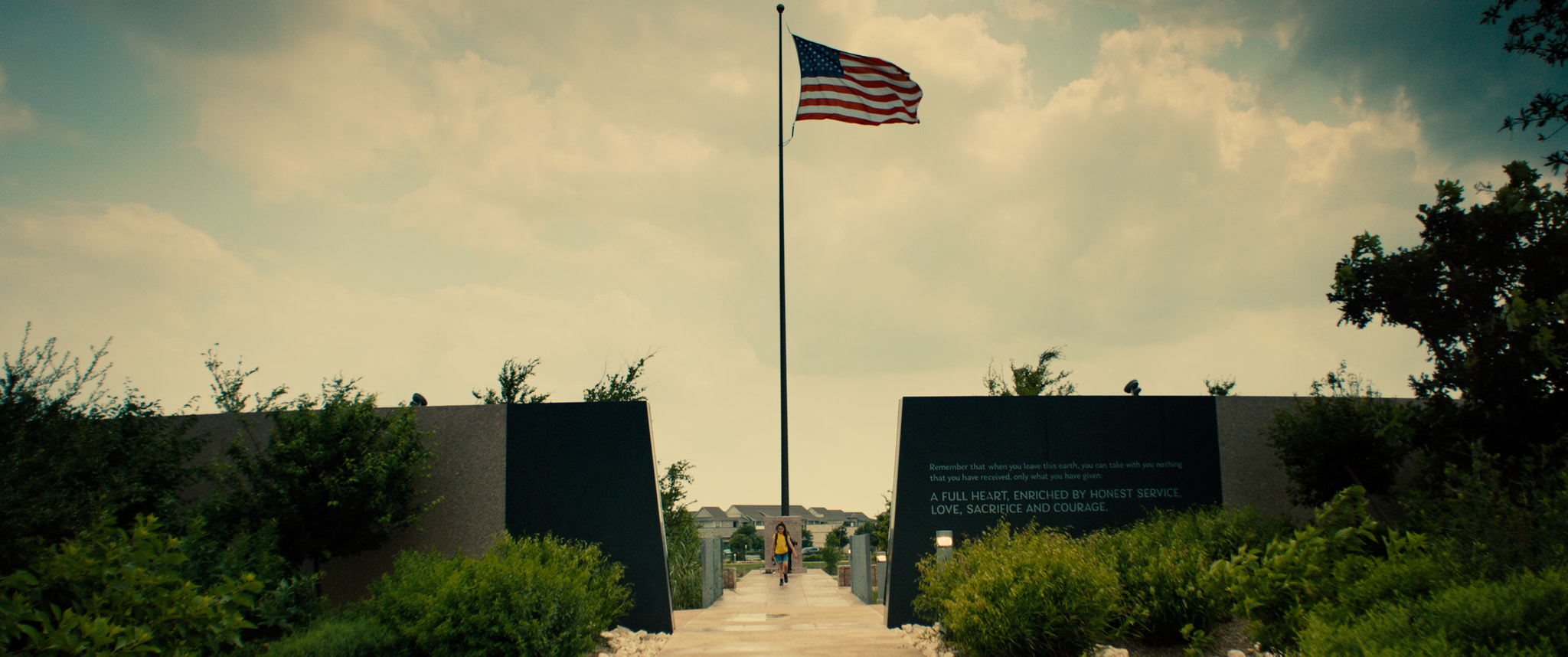 Ellie and George walk away from a memorial under an American flag